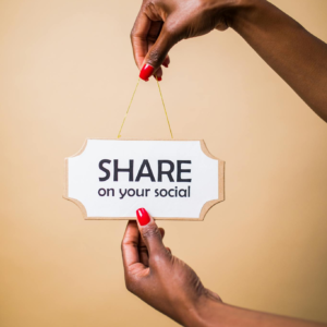 Close-up of a person's hand holding a 'Share on your social' sign against a beige background.